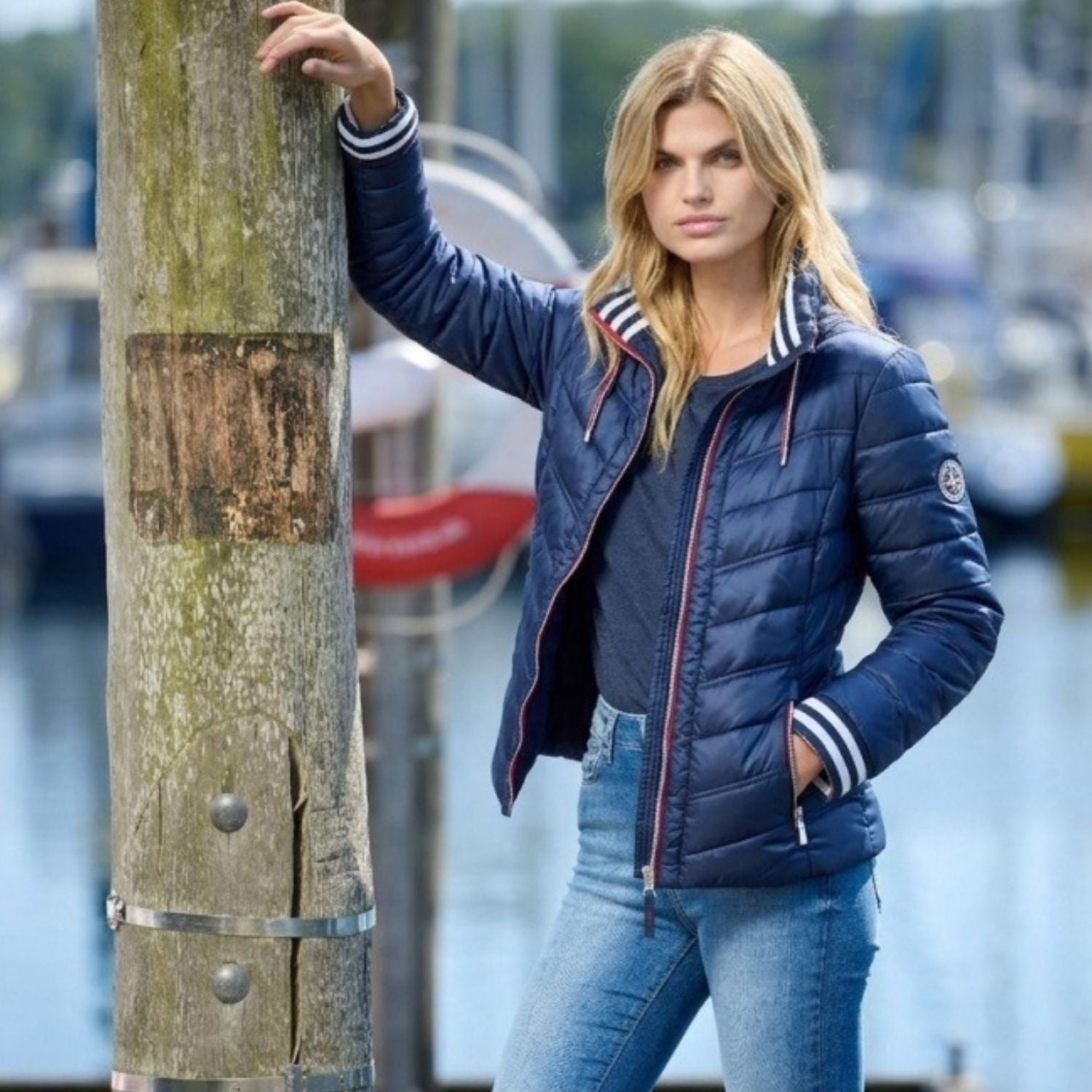 Dam i navy quiltad sommarjacka med randiga ribbkanter vid hamn som visar sommarjacka-trender 2026.