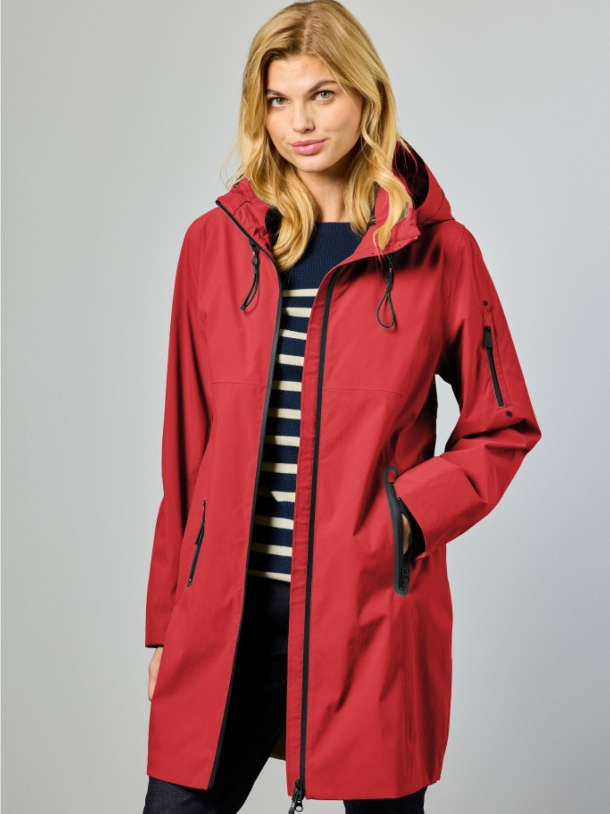 Nynne är en lång funktionsjacka för dam i röd med sportig silhuett och tydligt uttryck för våren.