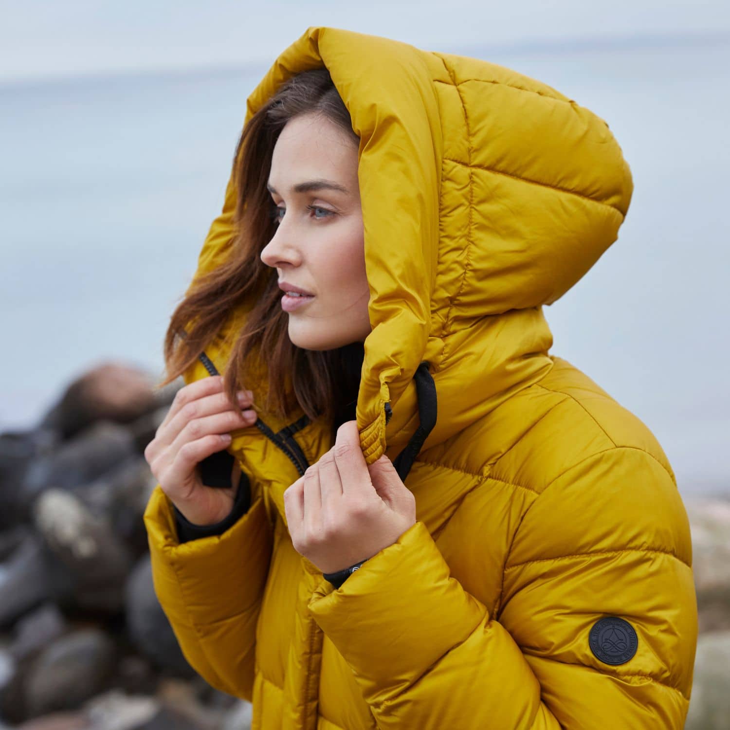 Modell i gul höstjacka med huva vid havet som visar höstens färger 2025 och säsongens jacks-trender