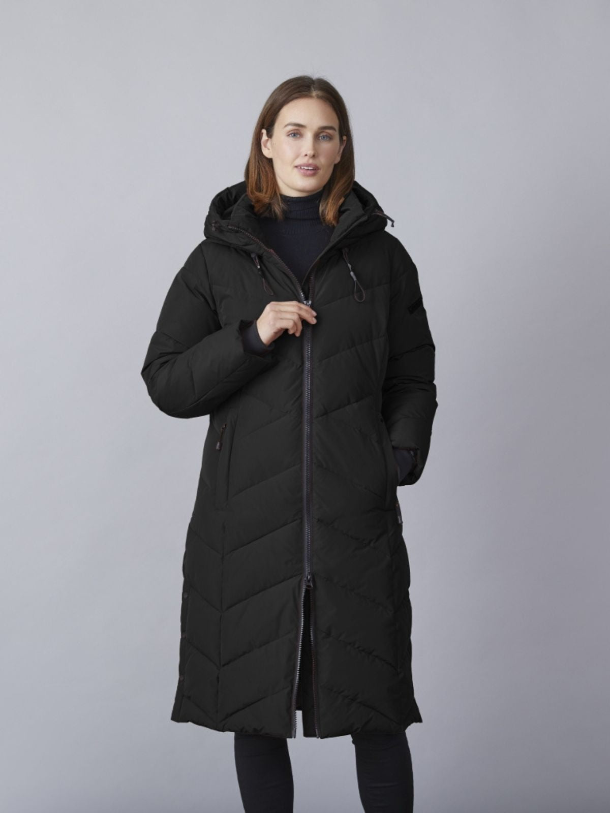 Modell iförd svart Katalin quiltad övergångsjacka för damer i lång comfort fit med huva och dragkedja.